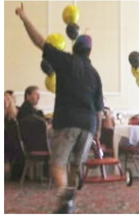 A strange man-boy wearing a beanie copter holds a tricycle in his right hand. He signals victory, pointing to the sky with his left index finger.